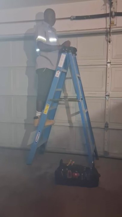 A student part way up a ladder, working on a garage door